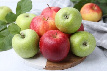 Fresh ripe apples and green leaves on light grey table, closeup