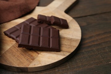 Pieces of delicious dark chocolate bar on wooden table, closeup. Space for text