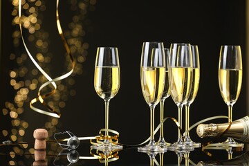 Champagne in glasses, bottle and cork on mirror surface against black background with blurred lights