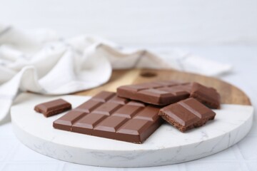 Pieces of delicious milk chocolate on white tiled table, closeup