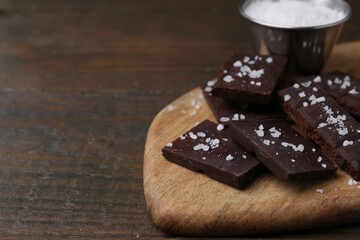 Pieces of chocolate with salt on wooden table, closeup. Space for text