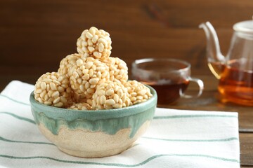 Delicious puffed rice balls in bowl and tea on wooden table, closeup