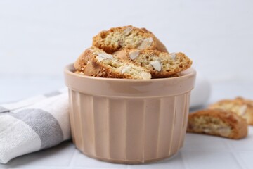 Tasty almond biscuits (Cantuccini) in bowl on white tiled table, closeup