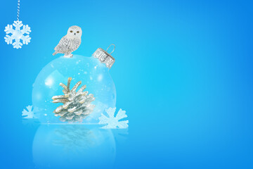 A pine cone inside a New Year's ball on a blue background. The owl is sitting on top. A Christmas card.