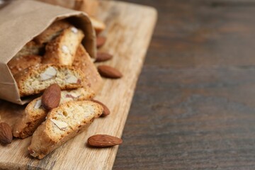 Paper bag with tasty almond biscuits (Cantuccini) and nuts on wooden table, closeup. Space for text