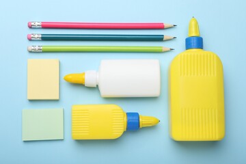 Bottles of glue, pencils and notes on light blue background, flat lay