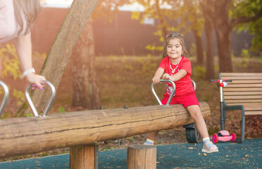 A little girl in the park swings on a balance swing (seesaw or teeter-totter)