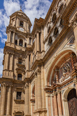 Fragments of majestic facade of Malaga Cathedral (1782), Baroque and Renaissance architecture with grand columns, detailed carvings, and archways under a clear blue sky. Malaga, Andalusia, Spain.