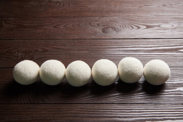 Six white wool dryer balls arranged in a straight line on a dark wooden surface with visible grain...