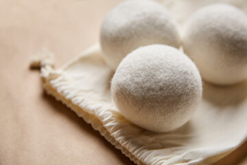 Close-up of three white wool dryer balls resting on an open cotton drawstring bag against a soft brown background, highlighting eco-friendly laundry essentials