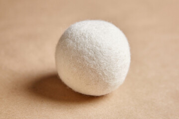 Close-up of a single, soft wool dryer ball against a beige background, showcasing texture and eco-friendly design, ideal for sustainable laundry use