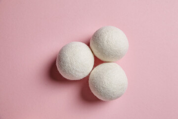 Three white wool dryer balls arranged in a triangle on a pastel pink background, showcasing their soft texture. Eco-friendly laundry alternative with minimalist appeal
