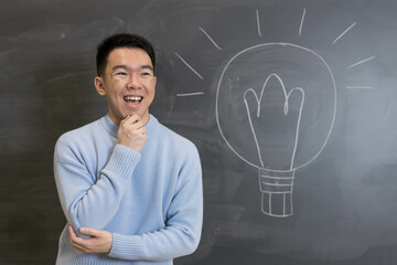 Young student smiling and thinking in front of a blackboard with a lightbulb