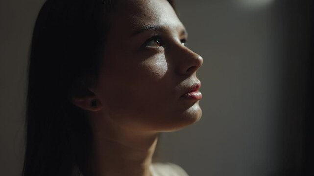 Close portrait of a young beautiful, attractive woman in the dark with the rays of the sun in her eyes, emphasis on facial features, study, work, reflections, fatigue, melancholy, depression, eye