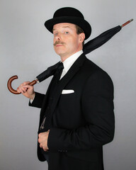 English Gentleman in Dark Suit and Bowler Hat Holding Umbrella Over His Shoulder. Vintage Style of Classic British City Businessman.