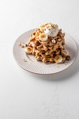 Homemade waffles stack with ice cream, bananas and nuts on white plate isolated on white background, text space