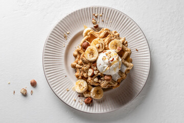 Homemade waffles stack with ice cream, bananas and nuts on white plate isolated on white background top view, text space