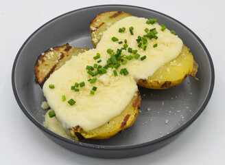 Baked potatoes with cheese and chives on a plate isolated on white