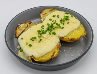 Baked potatoes with cheese and chives on a plate isolated on white