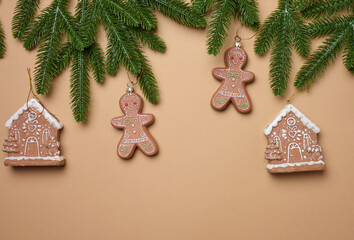 Spruce branches and Christmas tree decorations in the form of gingerbread houses and gingerbread men on a brown background