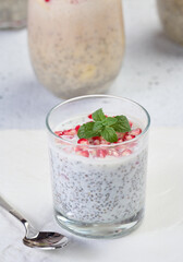 Glass with chia and yogurt dessert decorated with fresh fruits and pomegranate seeds on white table..