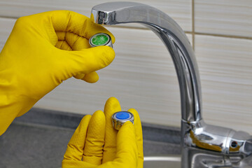 replacing a clogged faucet aerator with a new one. plumber in yellow rubber gloves holding an...