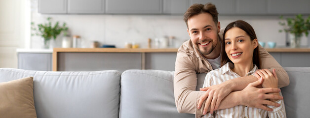 A joyful couple embraces on a comfortable couch in their stylish living room. Bright natural light fills the space, highlighting their warm smiles and the cozy decor around them.