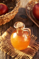 Unfiltered apple cider vinegar with red apples on a table in sunlight