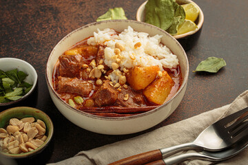 Hearty bowl of massaman curry features tender beef, potatoes, and fluffy rice, topped with crunchy peanuts and a fragrant cinnamon stick, showcasing the rich flavors of thai cuisine