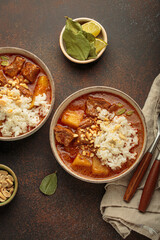 Two bowls of delicious massaman curry with peanuts, rice, herbs, lime, and spices on a brown background top view, dish of Thailand