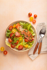 Grilled salmon fillet with fresh green lettuce, colorful cherry tomatoes salad top view, beige pastel background, healthy eating habits