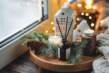 Natural Christmas essential oil, home aroma diffuser. Burning candles, branches of fir tree. Cinnamon, vanilla smell. Aromatherapy, cozy atmosphere, holiday festive mood. Close up macro, wooden table