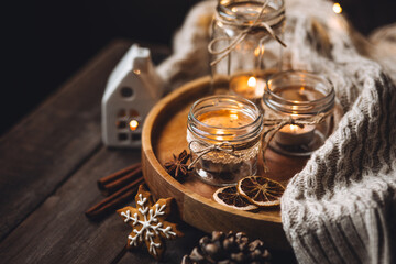 Cozy home holiday atmosphere. Idea for handmade christmas decorations: aromatic candles in glass jars. Cinnamon sticks, anise, dry citrus, homemade gingerbread cookies. Fairy lights