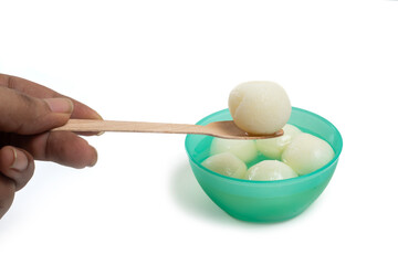 Close-up of hand taking traditional Indian dessert rasgulla from green bowl with wooden spoon