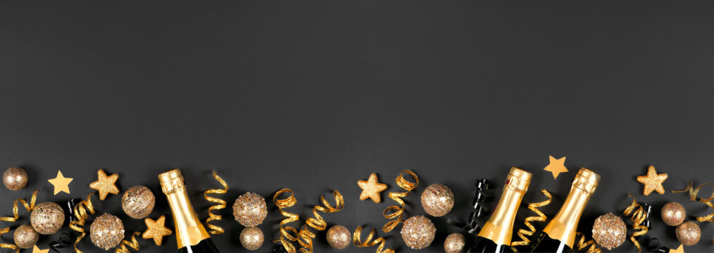 New Years Eve botom border of gold and black decorations, streamers and champagne. Top view over a black banner background.