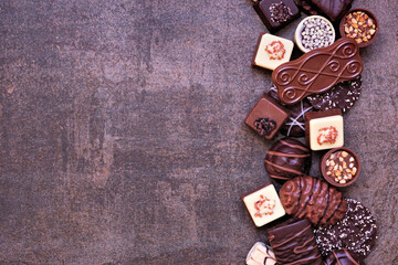 Chocolate side border with an assortment of fine, luxurious sweets. Top view on a dark stone background with copy space.