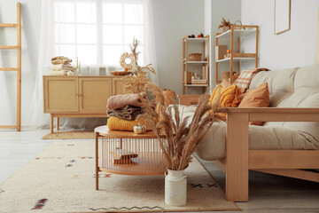 Stack of stylish clothes with autumn decorations on coffee table in living room