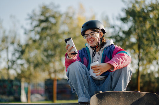 Smiling skater using smartphone and drinking coffee at skatepark - Powered by Adobe