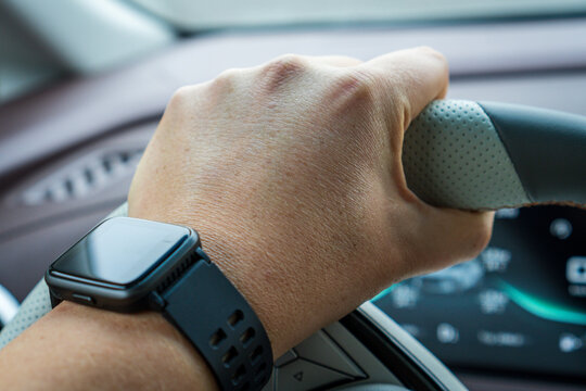 Hand of a man driving a modern car. Smart watch on wrist. The interior of a car full of technology with color displays and buttons.