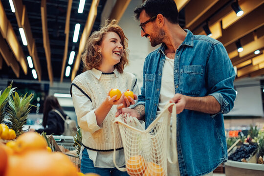 Happy couple choosing oranges in grocery store using reusable bag