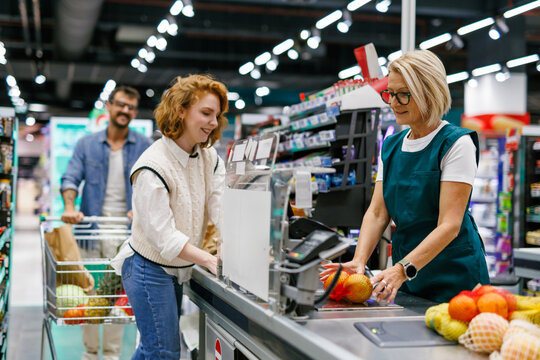 Cashier scanning groceries at supermarket checkout for smiling customer