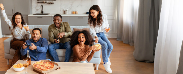 A group of multiracial friends gathers around in a bright living room, celebrating game night with...