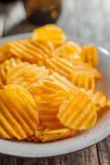 Crispy potato chips on plate on wooden table.