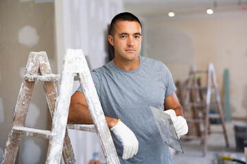 Portrait of man with float trowel standing at stepladder in apartment during repair works.