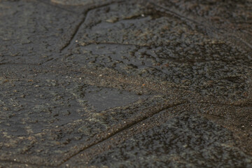 Macro shot capturing the detailed texture and patterns of a wet surface, highlighting the shimmering effects of water on rough, uneven stone