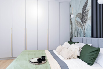 Interior of cozy bedroom with double bed with boho pillow in beautiful and minimalist indoors. Modern home and hotel room with textured wallpaper on the wall. Stylish architecture.