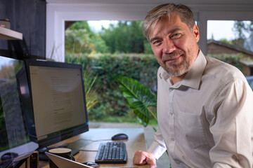 portrait d'un employé de bureau ou d'un homme d'affaires qui est assis à son bureau devant son ordinateur il est souriant et sympathique. Il est heureux de travailler chez lui à distance