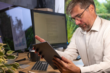 homme d'affaire ou employé de bureau de 50 ans souriant qui travaille avec une tablette. Il est en télétravail à la maison