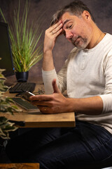 un homme de 50 ans est en télétravail chez lui dans son bureau devant son ordinateur. Il...