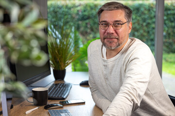portrait d'un employé de bureau ou d'un homme d'affaires qui est assis à son bureau devant son ordinateur il est souriant et sympathique. Il est heureux de travailler chez lui à distance